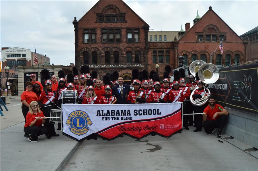  The band, staff, and Alabama Lions Club stand as a group with the ASB parade flag and smile.